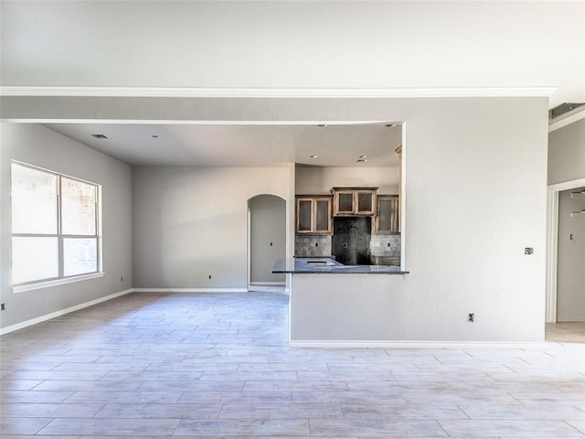 unfurnished living room with light wood finished floors, visible vents, arched walkways, and baseboards