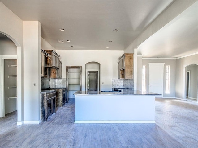 kitchen with arched walkways, baseboards, decorative backsplash, wood finished floors, and a peninsula