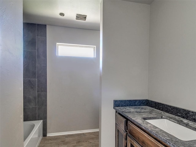 bathroom featuring a tub to relax in, wood finished floors, vanity, and baseboards