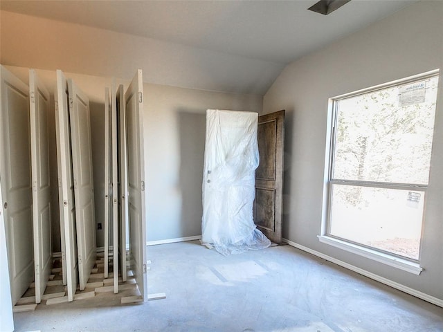 unfurnished room featuring vaulted ceiling, baseboards, and unfinished concrete floors