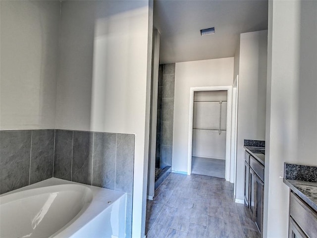 bathroom with a spacious closet, wood finished floors, vanity, and a bath