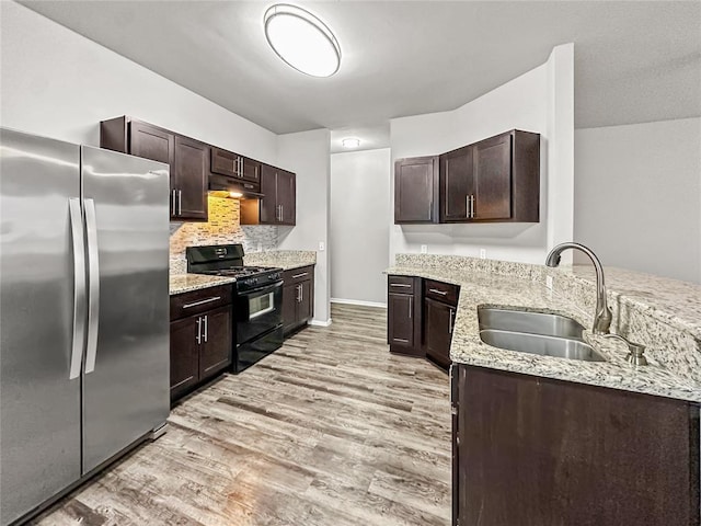 kitchen featuring black gas range oven, freestanding refrigerator, light wood-type flooring, under cabinet range hood, and a sink