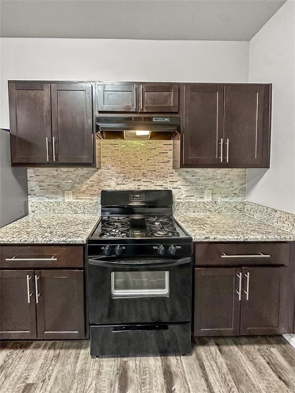 kitchen featuring black range with gas cooktop, under cabinet range hood, dark brown cabinets, light wood-type flooring, and decorative backsplash