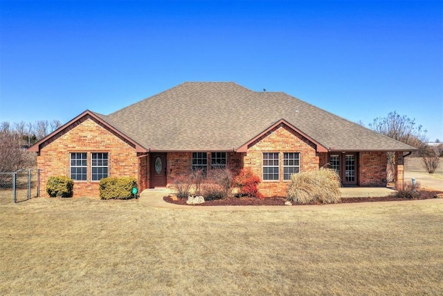 ranch-style home featuring brick siding, fence, roof with shingles, a gate, and a front yard