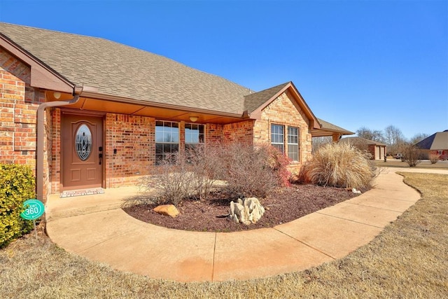 property entrance with roof with shingles and brick siding