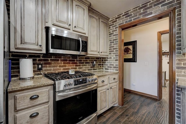 kitchen with baseboards, appliances with stainless steel finishes, dark wood-style flooring, light stone countertops, and backsplash