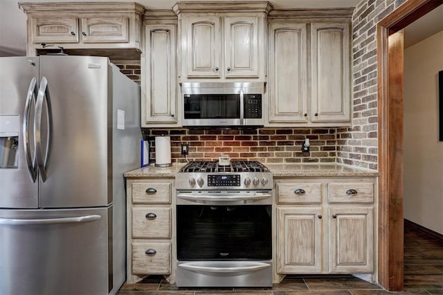 kitchen featuring stainless steel appliances, wood tiled floor, cream cabinetry, and light stone counters