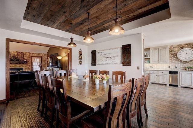 dining space with a fireplace, a raised ceiling, dark wood-type flooring, wood ceiling, and brick wall