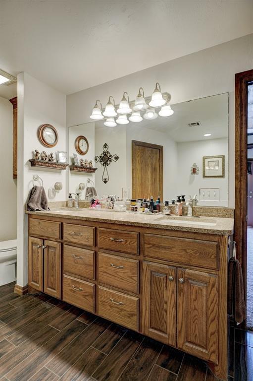 full bath with double vanity, visible vents, toilet, wood tiled floor, and a sink