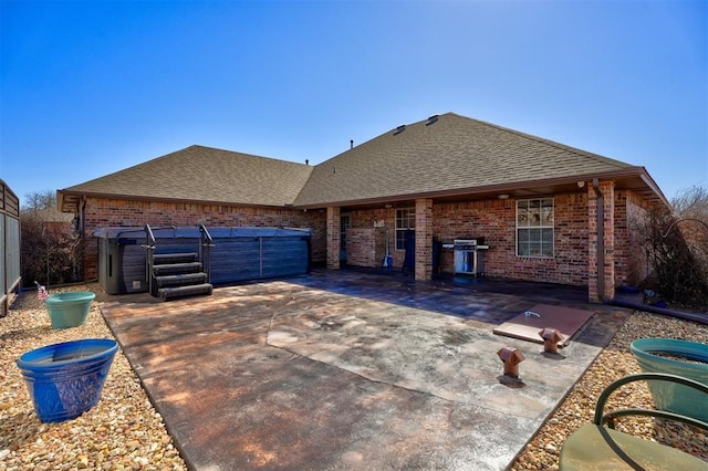 back of property featuring brick siding, a patio, and roof with shingles