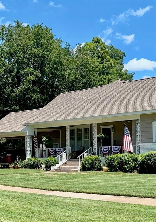 ranch-style house with covered porch, a shingled roof, brick siding, a carport, and a front lawn