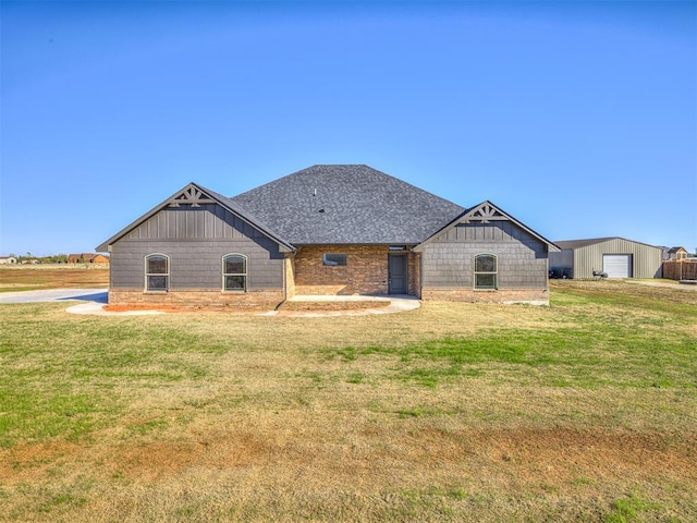 back of house featuring a garage, roof with shingles, a lawn, and an outdoor structure