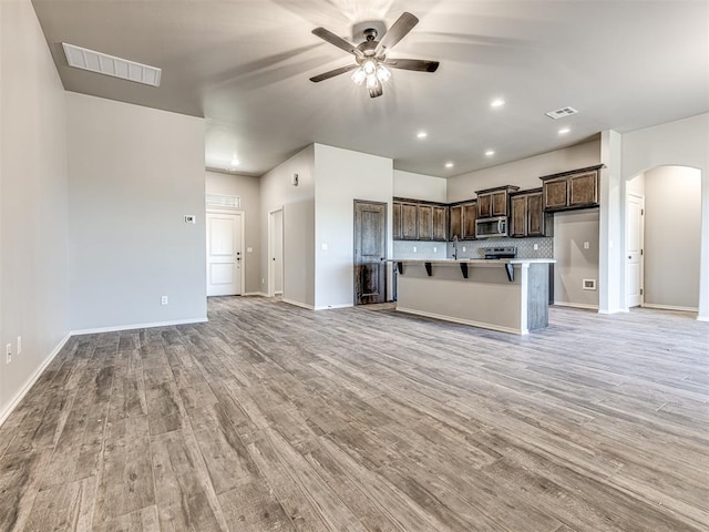 kitchen featuring arched walkways, stainless steel microwave, open floor plan, dark brown cabinets, and light wood-type flooring