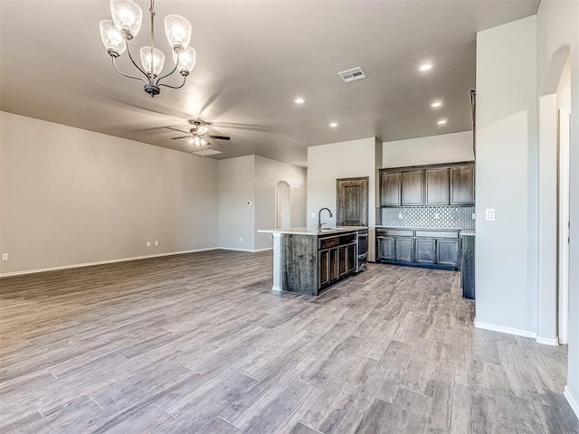 kitchen with visible vents, arched walkways, open floor plan, a sink, and ceiling fan with notable chandelier