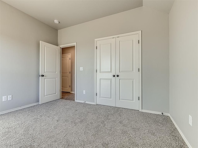 unfurnished bedroom featuring lofted ceiling, a closet, baseboards, and carpet flooring