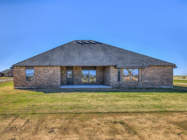 back of property featuring brick siding, a shingled roof, a lawn, and a patio