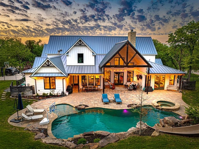 rear view of house with a standing seam roof, a patio, metal roof, an in ground hot tub, and a chimney