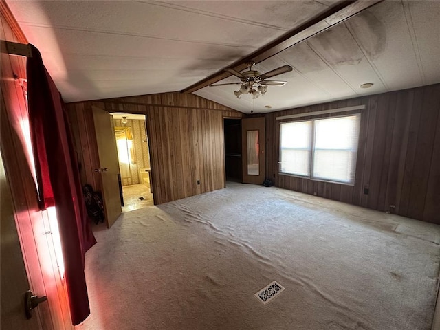 carpeted spare room with a ceiling fan, visible vents, vaulted ceiling with beams, and wood walls