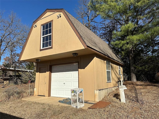 view of side of property featuring a garage, an outbuilding, roof with shingles, and a gambrel roof