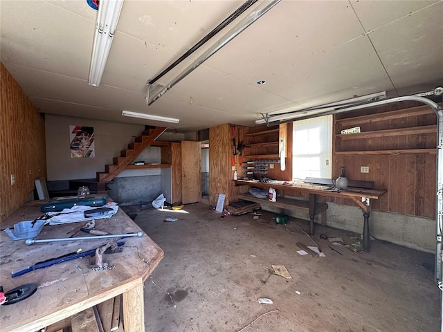 interior space with a workshop area, stairway, wooden walls, a garage, and concrete flooring