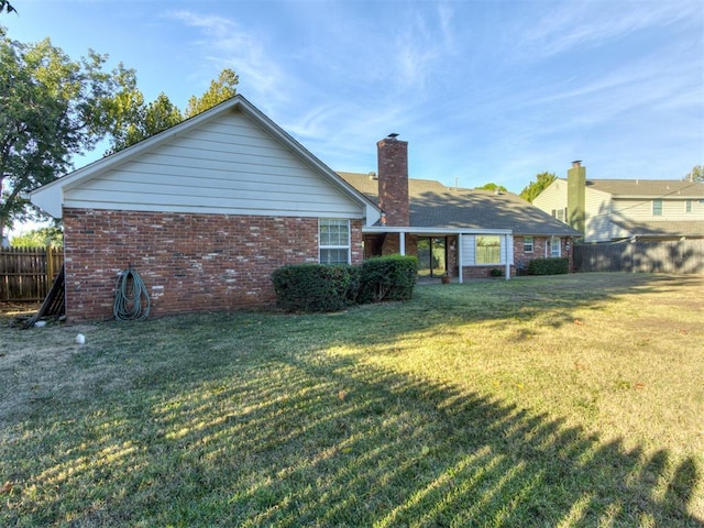 back of property with a yard, brick siding, fence, and a chimney