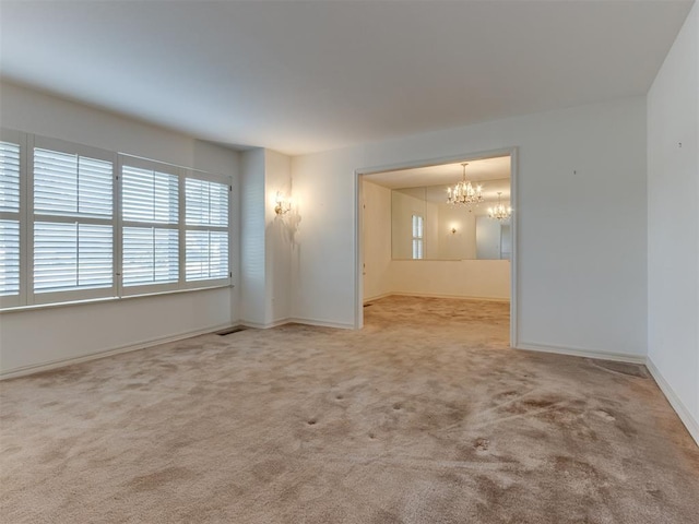 carpeted empty room featuring a notable chandelier and baseboards