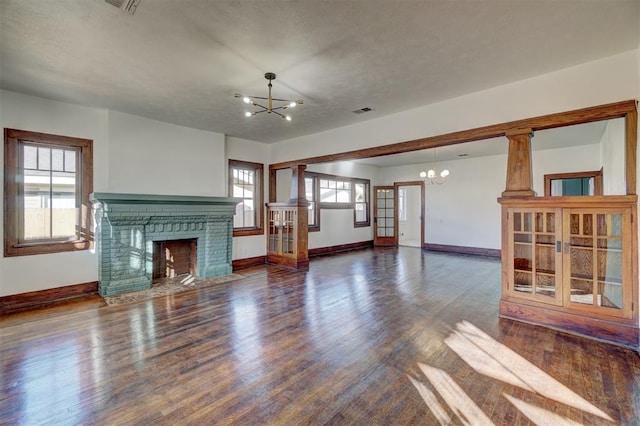 unfurnished living room with a brick fireplace, visible vents, a notable chandelier, and wood finished floors