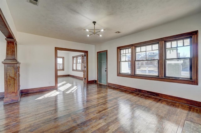 spare room featuring a chandelier, wood finished floors, visible vents, and baseboards