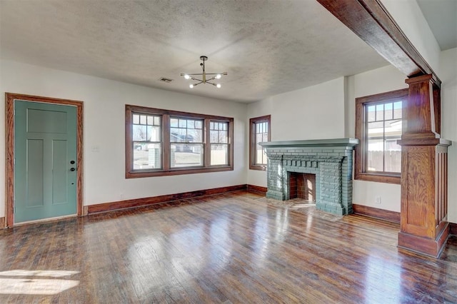 unfurnished living room with a brick fireplace, a textured ceiling, baseboards, and wood finished floors