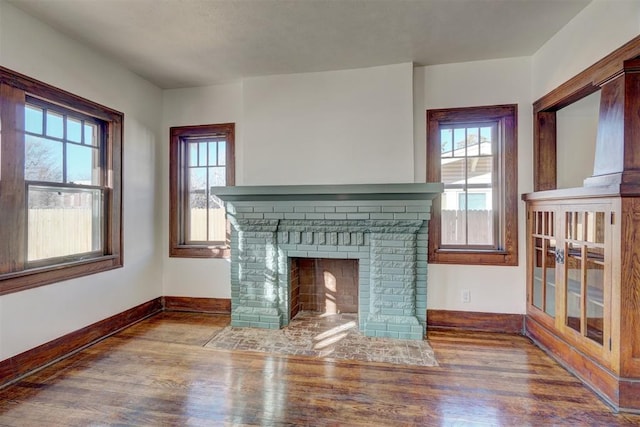 unfurnished living room featuring a fireplace, baseboards, and wood finished floors