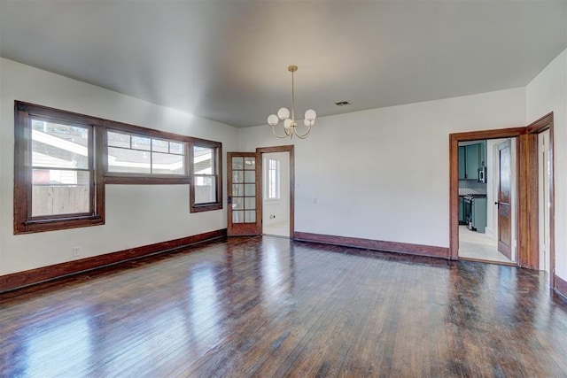 empty room with baseboards, wood finished floors, visible vents, and an inviting chandelier