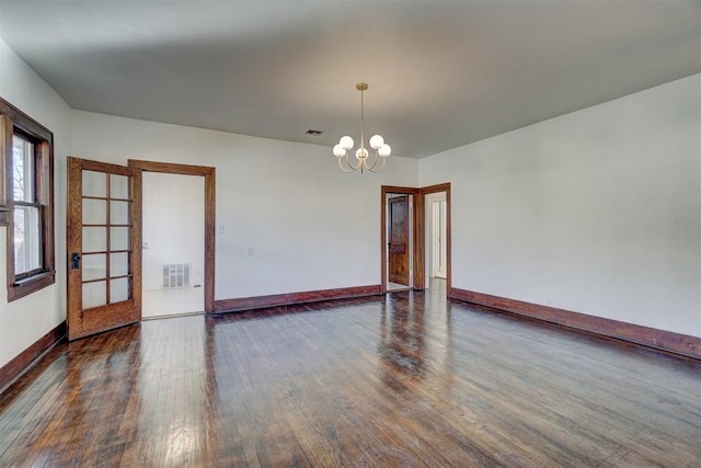 unfurnished room featuring a notable chandelier, baseboards, visible vents, and wood finished floors