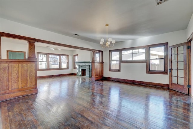 unfurnished living room with an inviting chandelier, a fireplace, baseboards, and dark wood finished floors