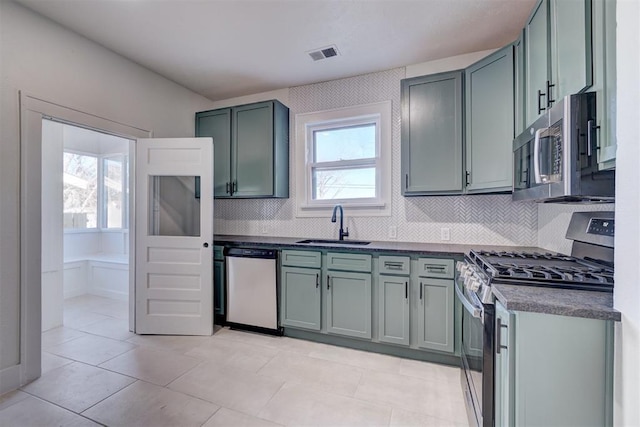 kitchen featuring stainless steel appliances, a sink, visible vents, decorative backsplash, and dark countertops