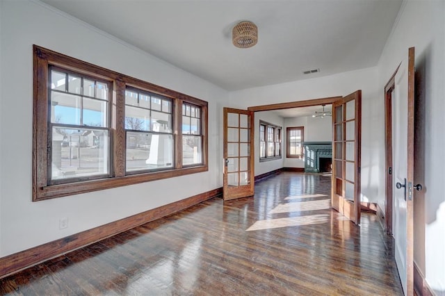 empty room featuring baseboards, visible vents, wood finished floors, a lit fireplace, and french doors