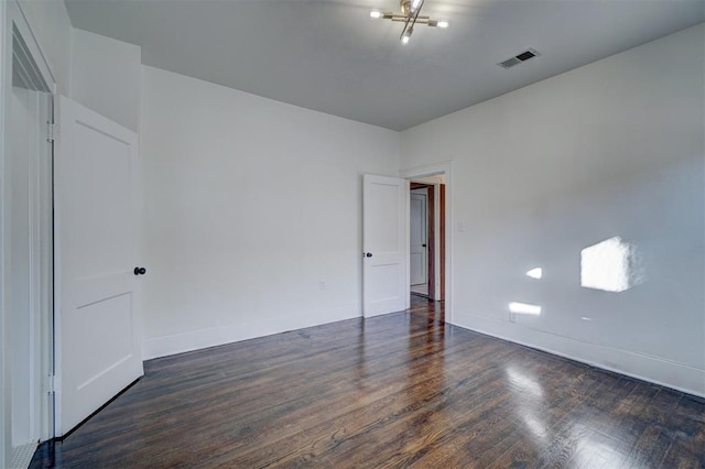 unfurnished room featuring a chandelier, dark wood-type flooring, visible vents, and baseboards