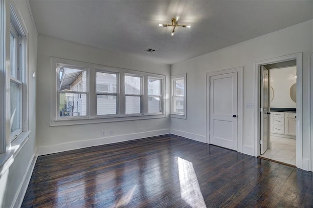 empty room featuring wood finished floors, visible vents, and baseboards