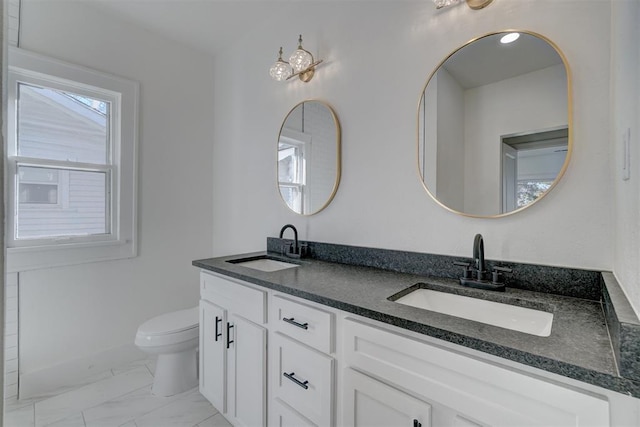 full bath with toilet, marble finish floor, double vanity, and a sink