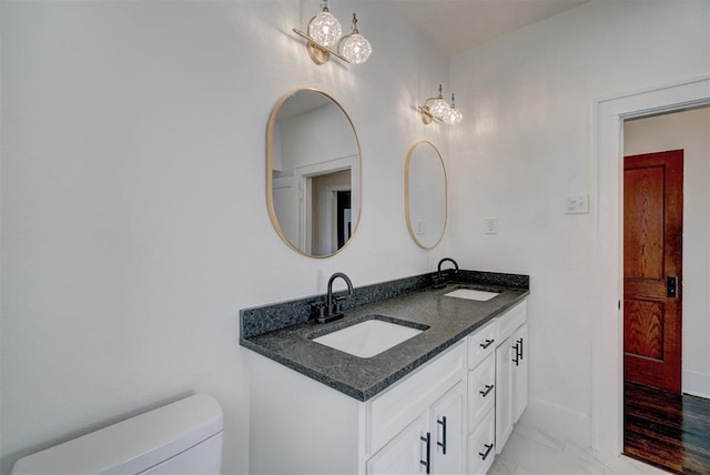 bathroom featuring toilet, marble finish floor, double vanity, and a sink