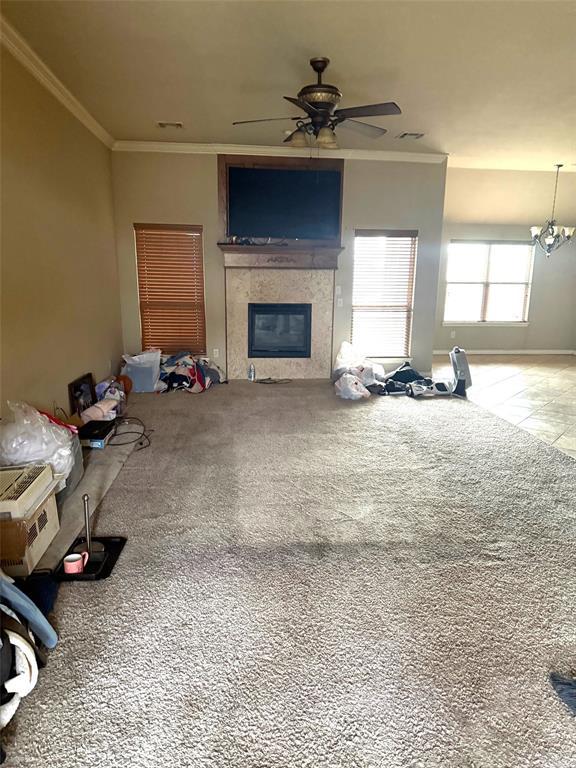 unfurnished living room with carpet, ceiling fan with notable chandelier, ornamental molding, and a glass covered fireplace