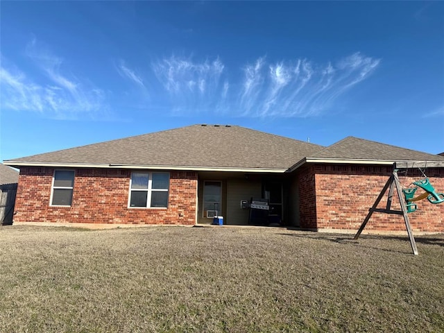 rear view of house with a yard, brick siding, a playground, and a shingled roof