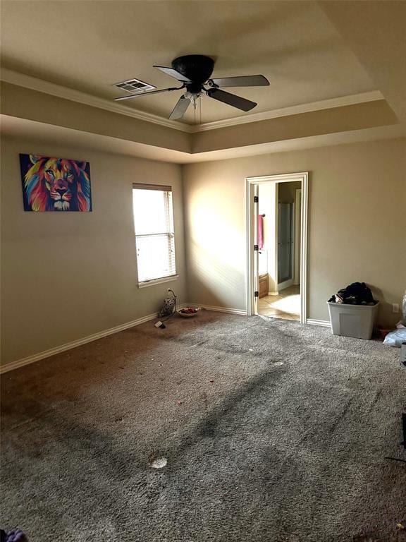 carpeted empty room with baseboards, visible vents, a ceiling fan, a raised ceiling, and crown molding