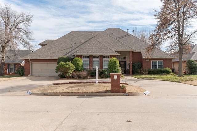 traditional home with a shingled roof, concrete driveway, brick siding, and an attached garage