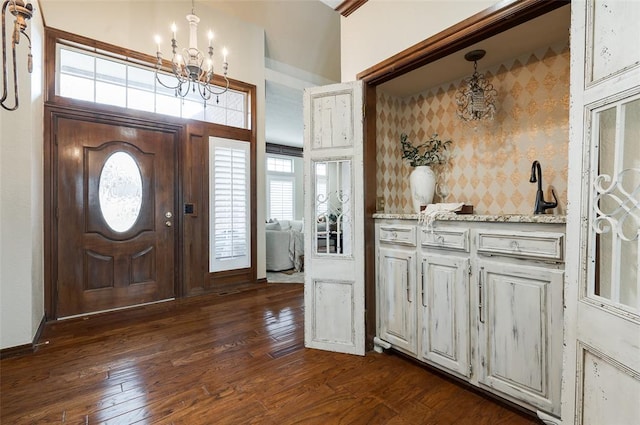 entrance foyer with dark wood-style floors, wallpapered walls, and a notable chandelier