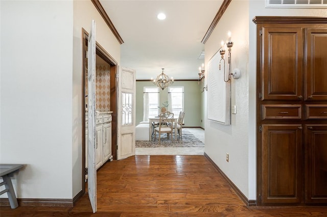 hallway featuring a notable chandelier, baseboards, ornamental molding, and wood finished floors