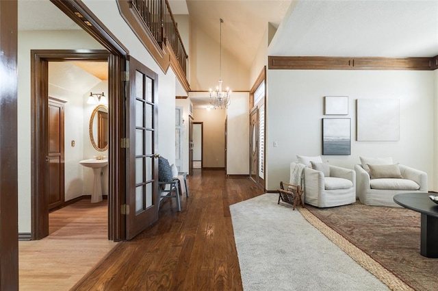 hallway featuring dark wood-style floors, baseboards, a towering ceiling, and a notable chandelier