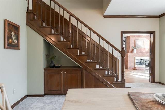 staircase featuring crown molding, carpet floors, a brick fireplace, and baseboards