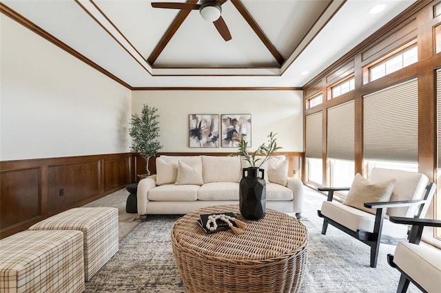 living area featuring ceiling fan, light colored carpet, a wainscoted wall, a high ceiling, and ornamental molding