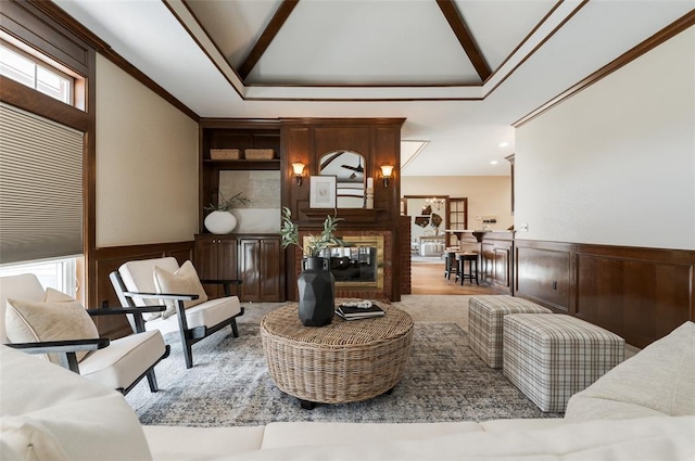 living area featuring crown molding, a fireplace, a decorative wall, wainscoting, and high vaulted ceiling