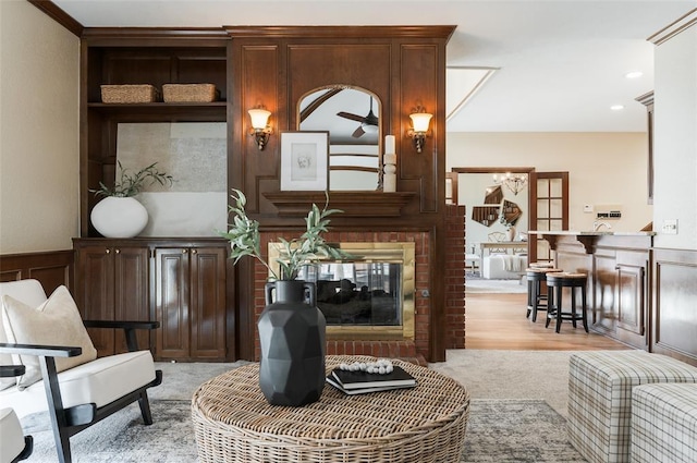 living area with a brick fireplace, a decorative wall, light colored carpet, and wainscoting